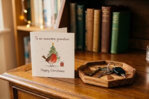 A Christmas card reading "To an awesome grandson" sitting on a wooden surface next to a key tray with keys.